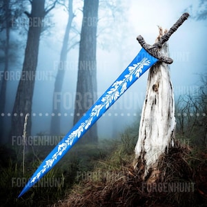 May include: A large, blue sword with a white leaf design on the blade. The hilt is dark and intricately detailed. The sword is leaning against a weathered tree stump in a misty forest setting.
