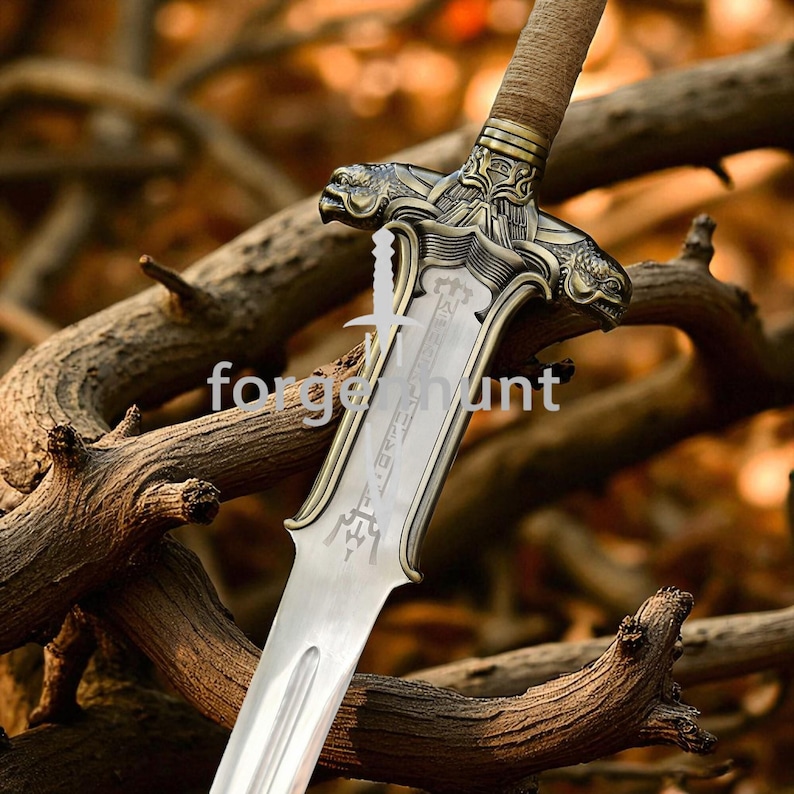 May include: A detailed close-up of a sword with a silver blade and ornate bronze hilt. The hilt features two dragon-like figures and intricate carvings. The text "forge hunt" is visible on the blade. The sword is set against a blurred background of tree branches.