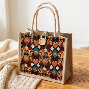 May include: A small tote bag with a geometric pattern in shades of red, orange, green, and black. The bag has a natural jute exterior, rope handles, and a wooden button closure. The bag is designed for carrying small items.