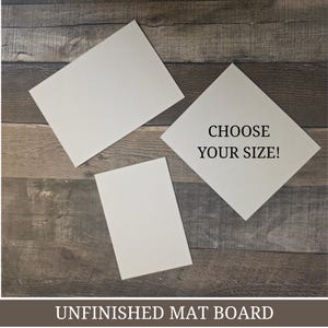 Puede incluir: Tres cartones de paspartú blancos sin terminar de diferentes tamaños están dispuestos sobre una superficie de madera. Uno de los cartones tiene el texto "CHOOSE YOUR SIZE!". La parte inferior de la imagen tiene el texto "UNFINISHED MAT BOARD".