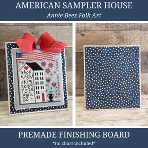 May include: A framed sampler with a patriotic theme, featuring a stitched house, American flag, and decorative elements. The frame is adorned with a red bow. The text "AMERICAN SAMPLER HOUSE" and "PREMADE FINISHING BOARD" are visible.