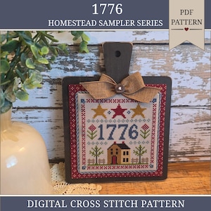 May include: A square wooden board with a handle features a cross-stitch sampler titled 1776 Homestead Sampler Series. The sampler displays the year 1776, stars, flowers, trees, and a house, accented by a tan burlap bow and a small button.