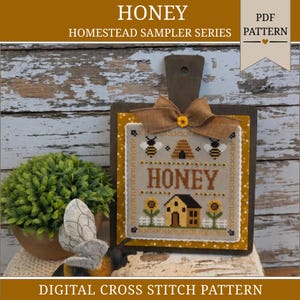 May include: A cross stitch pattern titled HONEY HOMESTEAD SAMPLER SERIES featuring a bee skep, bees, sunflowers, and a house. The design is mounted on a dark wooden board with a burlap bow and a small yellow flower accent at the top center.