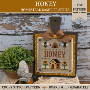 May include: A cross-stitch pattern on a square fabric piece mounted on a dark wooden board. The design features the text HONEY, two bees, a beehive, a house, and two sunflowers. A tan burlap bow with a small yellow flower sits at the top.