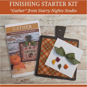 May include: A finishing starter kit titled Gather from Starry Nights Studio, featuring a printed instruction booklet and a dark brown wooden board. The kit includes a piece of orange and green plaid fabric, a green ribbon, and four small leaf-shaped embellishments in yellow, red, dark green, and orange.