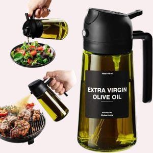 Puede incluir: Una botella de vidrio transparente con tapa y asa negras, etiquetada como "EXTRA VIRGIN OLIVE OIL". La botella se muestra vertiendo aceite sobre una ensalada y una parrilla. Contiene 470 ml.