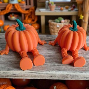 May include: Two orange pumpkin figurines with green stems and attached legs and feet. The pumpkins are sitting on a wooden surface, with other pumpkins visible in the background. These whimsical figurines are a fun decoration for autumn.