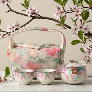 May include: A floral-patterned tea set with a matching tote bag. The set includes a teapot, two teacups, and a tote bag, all adorned with pink and peach flowers. The background features a branch with white and pink blossoms.