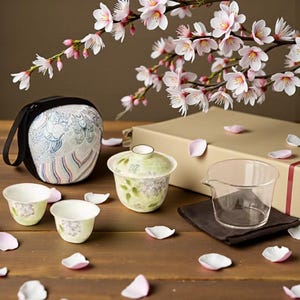 Può includere: Un set da tè a tema floreale, composto da una tazza da tè con coperchio, due tazzine e una caraffa in vetro. Il set è accompagnato da una custodia e una confezione regalo. Rami e petali di fiori di ciliegio aggiungono un tocco decorativo.