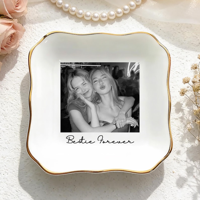 May include: A white ceramic trinket dish with a gold trim and a black and white photograph of two people embracing. The dish is inscribed with the words "Bestie Forever".