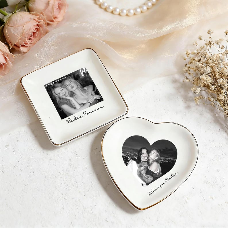 May include: Two decorative trinket dishes. One square dish and one heart-shaped dish. Both are white with gold trim and feature black and white photos. The square dish has the text "Bestie Forever". The heart dish has the text "Love you Bestie".