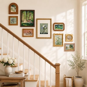 Peut inclure: Une composition murale de galerie comprenant neuf tirages d'art encadrés représentant divers paysages et sujets floraux, disposés sur un mur clair au-dessus d'un escalier en bois avec une rampe blanche, une console en bois et une plante en pot.