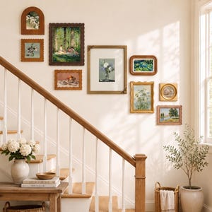 Puede incluir: Una pared de galería con diez pinturas e impresiones enmarcadas de diversas formas y tamaños, incluyendo marcos rectangulares, cuadrados y arqueados con acabados en madera, dorado y festoneado, dispuestos sobre una pared clara.