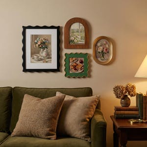 May include: A selection of framed art pieces, including a black wavy-edged frame with a floral still life, a wooden arched frame, a green wavy-edged frame, and an oval gold frame. The art is displayed above a green sofa with brown cushions.