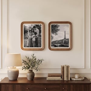 May include: Two rectangular wooden picture frames with rounded corners, each containing a black and white photograph. One frame displays a family of four outdoors, while the other shows a view of the Eiffel Tower in Paris across a river.
