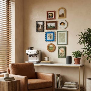 Puede incluir: Una pared de galería con nueve marcos de fotos variados de diferentes formas y colores, incluyendo diseños rectangulares, ovalados y festoneados, dispuestos sobre una mesa consola con una cafetera, libros y un altavoz inteligente.