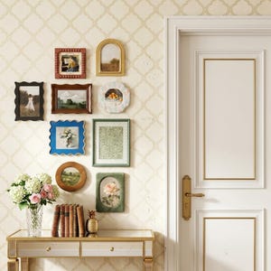 May include: A collection of framed art pieces in various shapes and sizes adorns a wall. The frames are in shades of brown, black, blue, and green, with artwork depicting landscapes, still lifes, and floral arrangements. A mirrored console table with a vase of flowers and books sits below.