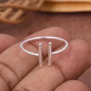 Op de afbeelding: Een minimalistische zilveren ring met twee verticale staafjes. De ring is dun en delicaat, met een eenvoudig, modern ontwerp. De staven zijn gelijkmatig verdeeld en geven de ring een unieke uitstraling.