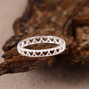 May include: A silver-toned ring featuring a continuous band of cut-out heart shapes. The metal has a polished finish, and the design consists of a repeating pattern of open hearts encircling the entire circumference of the circular band.