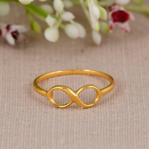 Op de afbeelding: Een goudkleurige ring met een centraal oneindigheidssymbool. De band is dun en glad en heeft een gepolijste metalen afwerking die het licht reflecteert. Het oneindigheidsmotief is direct in de ronde bandstructuur verwerkt.