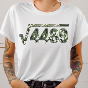 May include: White t-shirt with a square root symbol above the number 4489. The graphic is a camouflage pattern in green, brown, and beige. The shirt has short sleeves and a round neck.