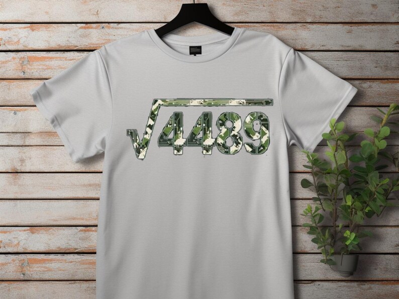 May include: A light grey t-shirt with a square root symbol over the number 4489. The numbers and symbols are in a camouflage pattern of green, brown, and white. The shirt is hanging on a black hanger.