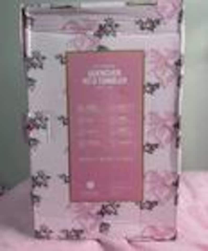 May include: A rectangular box with a pink and white floral pattern. The box has a pink label with text that reads "Lavender Bath & Body Collection". The box is white with a handle at the top.