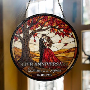 Può includere: Pannello rotondo in vetro colorato con cornice in metallo nero, raffigurante una coppia che si bacia sotto un albero con foglie autunnali. Il testo recita "40th Anniversary" con i nomi "David & Sophia" e la data "02.08.1985".