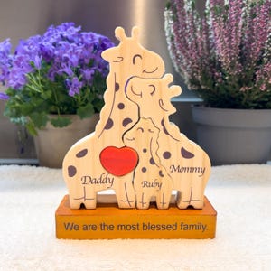 May include: Wooden family giraffe sculpture with a red heart and the words "Daddy," "Ruby," and "Mommy." The base reads "We are the most blessed family." The giraffes have brown spots and are on a wooden base.