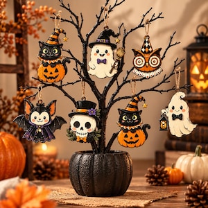 May include: A black decorative tree in a pumpkin-shaped pot, adorned with seven hanging Halloween ornaments: two black cats in pumpkins, two ghosts, one owl, one bat, and one skull, all featuring colourful details and attached with twine loops.