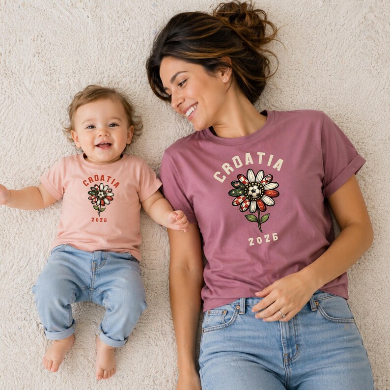 May include: A light pink t-shirt and a mauve t-shirt, both featuring a graphic of a flower with a soccer ball center, the text "CROATIA" arched above, and "2025" below. The flower petals incorporate red and white checkered patterns.