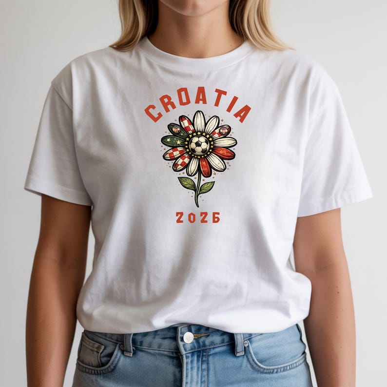 May include: A white t-shirt featuring a graphic of a flower with petals patterned in red and white checkers and green accents. A soccer ball sits at the center of the flower. The text CROATIA is arched above the flower, and 2026 is printed below.