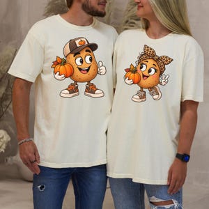 May include: Two cream-colored t-shirts featuring cartoon potato characters. The left shirt shows a potato wearing a baseball cap and sneakers holding a pumpkin. The right shirt shows a potato with a leopard print bow and sneakers holding a pumpkin.