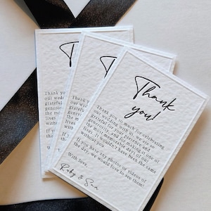 May include: Three white rectangular thank you cards with black text and a black ribbon. The cards have the words "Thank you!" in a script font and a message thanking guests for attending a wedding.