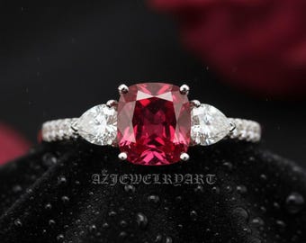 May include: A close-up of a three-stone ring with a large, square, red gemstone as the center stone. Two pear-shaped white gemstones flank the center stone. The band is encrusted with small, clear gemstones. The text "AZJEWELRYART" is visible.