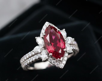 May include: A marquise-cut ruby ring with a halo of small diamonds and a double band. The ruby is a deep red color, and the diamonds sparkle. The ring is set in a silver metal.
