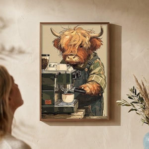 Op de afbeelding: Een ingelijste kunstdruk toont een Schotse Hooglandkoe die koffie zet. De koe draagt een overall en een groen en beige gestreept overhemd. De koffiemachine is groen en zilver. De print hangt aan een beige muur.