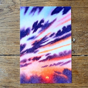 May include: Watercolor painting of a sunset with a vibrant sky. The sky transitions from light blue to pink and orange, with dark purple cloud formations. A small, bright orange sun is visible.