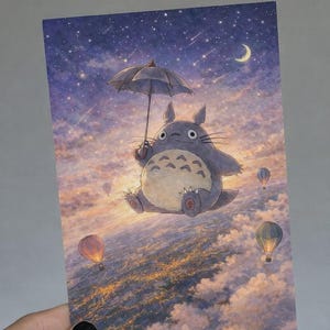 May include: A postcard featuring a whimsical illustration of a gray, round creature holding an umbrella, floating above clouds with hot air balloons. The background shows a starry sky and a crescent moon.