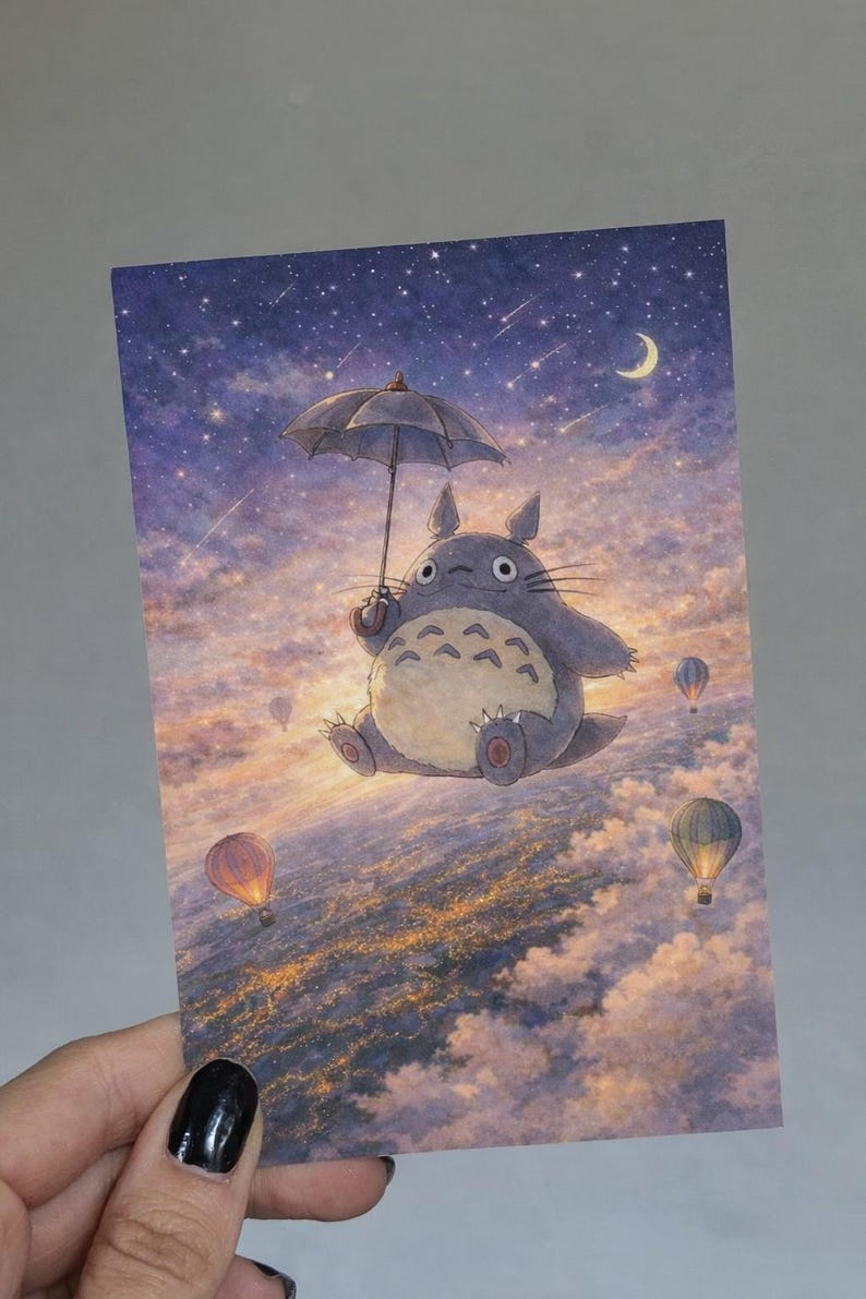 May include: A postcard featuring a whimsical illustration of a gray, round creature holding an umbrella, floating above clouds with hot air balloons. The background shows a starry sky and a crescent moon.