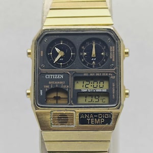 May include: A gold Citizen watch with a black rectangular face. It has two analog dials, a digital display showing time and temperature, and the text "ANA-DIGI TEMP". The watch band is gold. The temperature is displayed in Celsius.