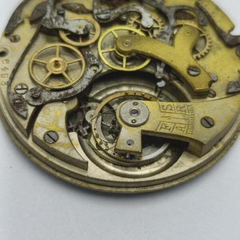 May include: Close-up of a vintage watch movement, showcasing intricate gears and mechanisms. The metal components are in shades of gold and silver, with visible text and small screws. The overall aesthetic suggests a focus on antique timepieces and horology.