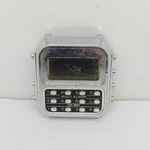 May include: A vintage silver digital watch with a rectangular face. The watch features a cracked screen and multiple buttons labeled with numbers and functions like "MULTI ALARM" and "PM". The model number "CA-951" is also visible.
