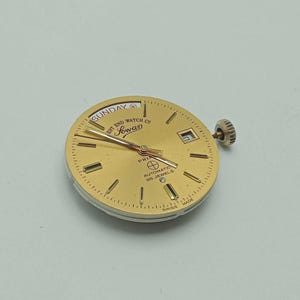 May include: A gold-toned watch face with the text "Sunday" and "West End Watch Co." The watch face has gold hands and markers, a date window, and the text "Sowan". The watch is marked "Automatic 25 Jewels" and "Swiss Made".