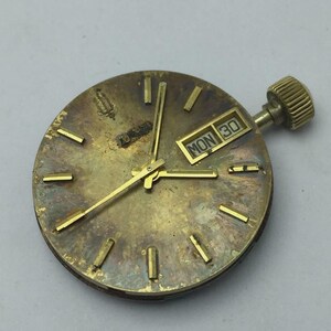 May include: A vintage watch face with a gold-toned finish, featuring gold hands and hour markers. The date display shows "MON 30." The watch crown is visible on the right side. The watch face has a worn, aged appearance.