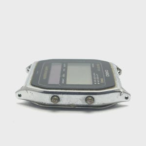 May include: A vintage Casio digital watch with a silver-tone metal case and a black display. The watch face has multiple digital readouts and buttons. The word "CASIO" is printed on the watch face.