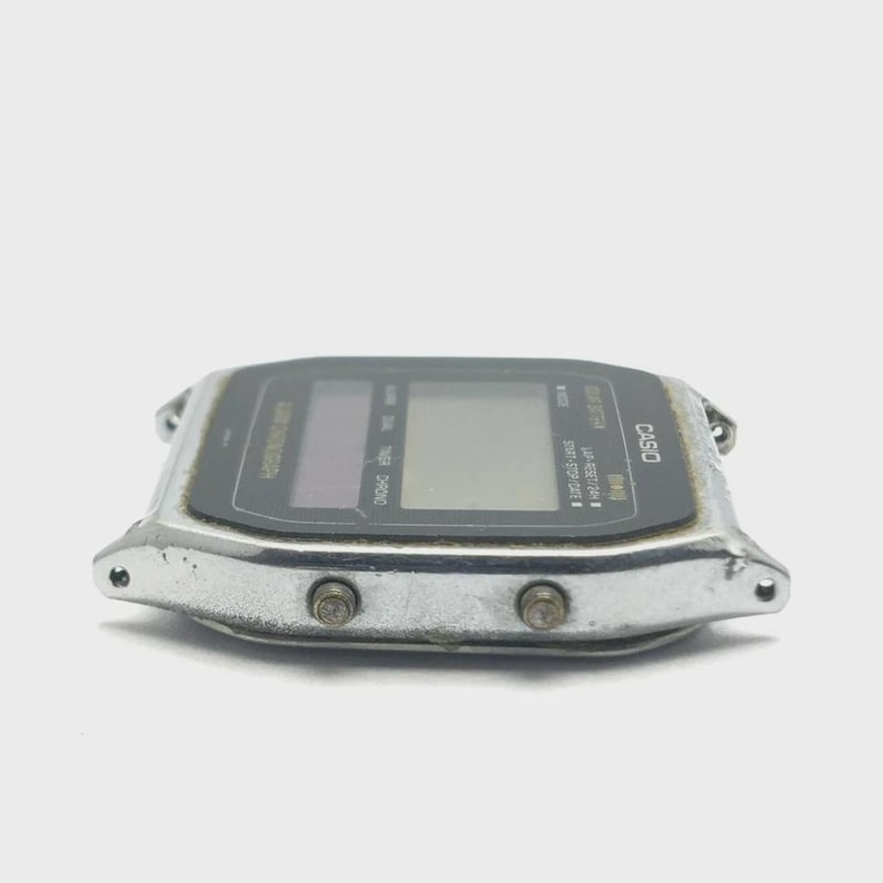 May include: A vintage Casio digital watch with a silver-tone metal case and a black display. The watch face has multiple digital readouts and buttons. The word "CASIO" is printed on the watch face.