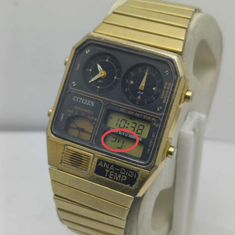 May include: A gold-coloured Citizen Ana-Digi Temp watch. The black watch face features analog dials and a digital display showing the time and temperature. The watch strap is also gold-coloured.