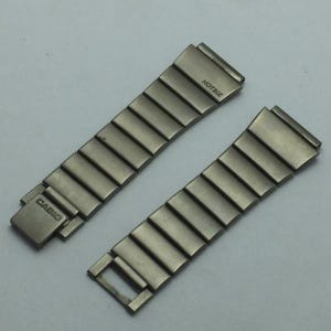 Puede incluir: Dos correas de reloj plateadas. Una correa tiene un cierre con la palabra "CASIO" grabada. La otra correa tiene la palabra "HOTBIZ" grabada. Ambas correas est&aacute;n hechas de eslabones met&aacute;licos rectangulares.