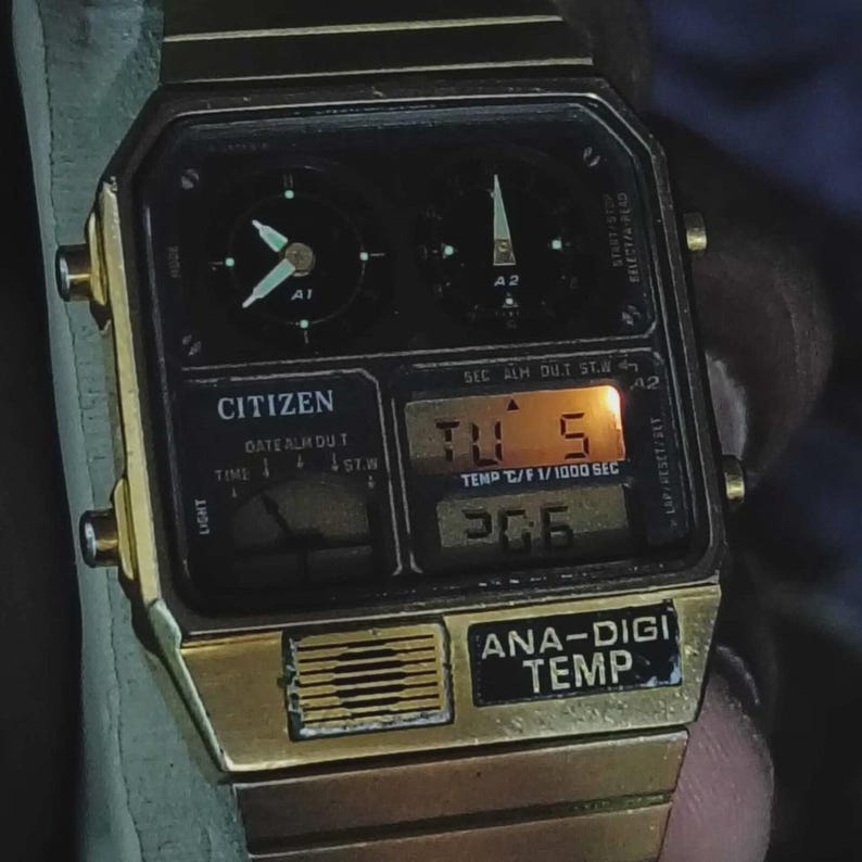 May include: A gold-coloured Citizen Ana-Digi Temp watch. The watch face is black with digital and analogue displays. The digital display shows "TU 5" and "306". The watch has a gold-coloured metal strap.